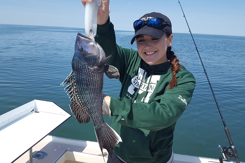 Fishing Charters Young Woman Holding a Sea Bass She Caught on the Flying Connie